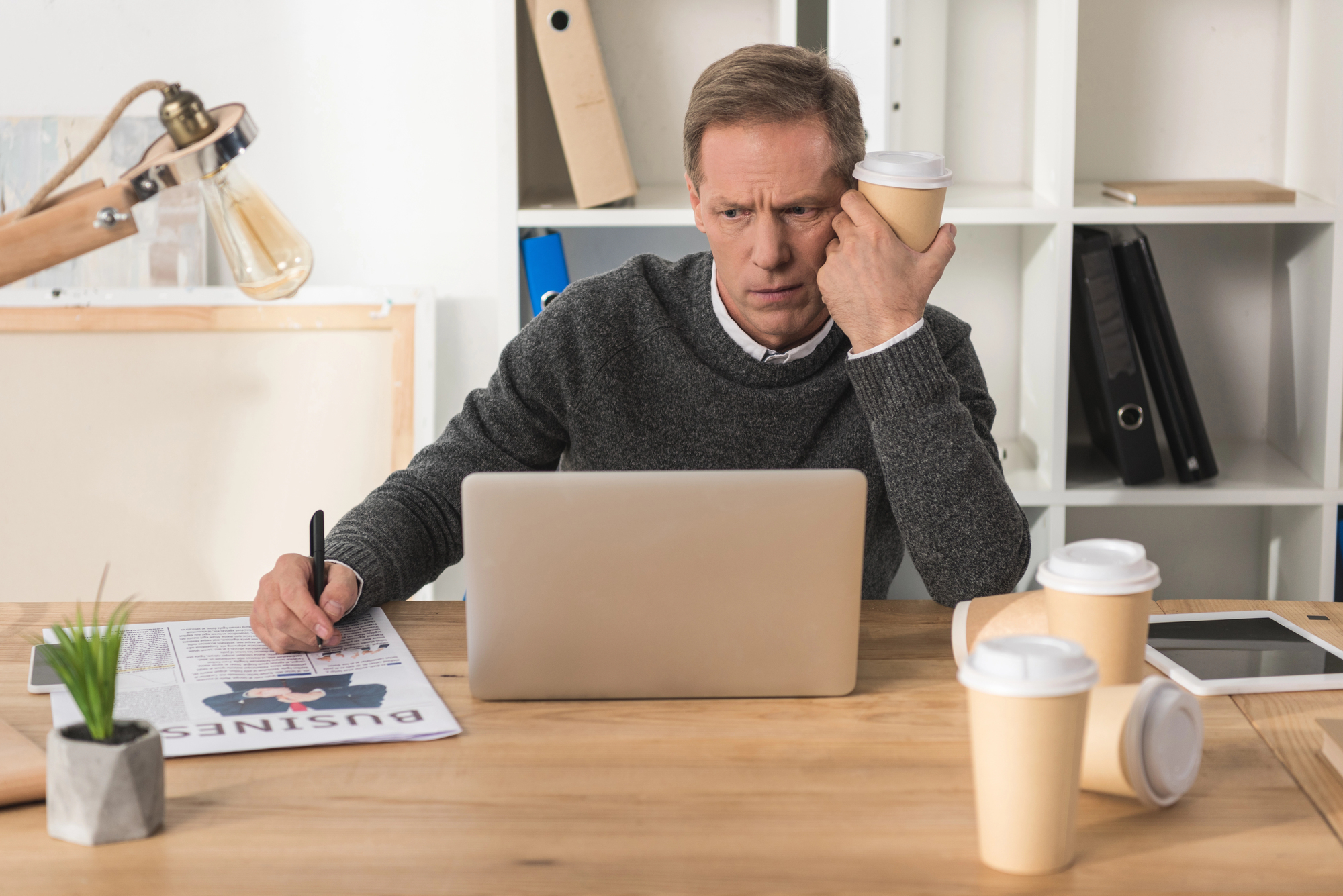 Tired businessman sitting at laptop with disposable coffee cup