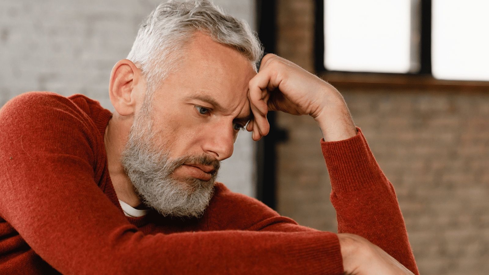 A middle-aged man sitting on a couch in the evening, visibly drained